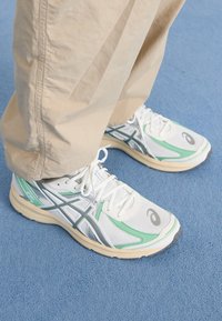 Vita och mintgröna löparskor med mesh-övre, gummisula och grå detaljer. Har snören och logotyp på sidan.