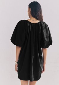 Sort linnedragt med puffede ærmer og en rynket halsudskæring, med løs pasform og knælængde. Enkel, elegant tekstur.