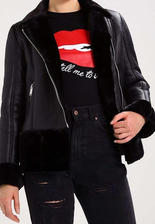 Sort læderjakke med imiteret pelskrave og manchetter, har sølvfarvede lynlåse, kort design, båret over en sort T-shirt med grafik og slidte jeans.