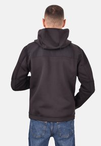 Zwarte hoodie met een hoge kraag, flexibele stof, naadloze schouders en aansluitende manchetten. Draagt over blauwe spijkerbroeken.