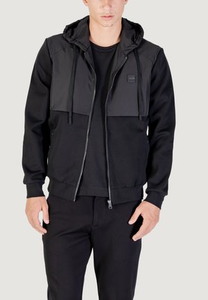 Black hoodie with a smooth texture and contrasting front panel, featuring a zip closure and adjustable drawstring hood. Simple design.