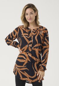 Chemise à manches longues, bleu marine avec un motif de feuilles orange, dotée d'une patte de boutonnage et d'incisions latérales pour faciliter les mouvements. Texture lisse.
