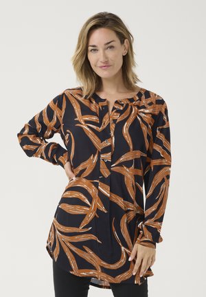 Chemise à manches longues, bleu marine avec un motif de feuilles orange, dotée d'une patte de boutonnage et d'incisions latérales pour faciliter les mouvements. Texture lisse.