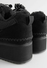 Zapatos de plataforma negros con parte superior de ante suave, ribete esponjoso y cordones negros. Detalles de costura en el talón y suela texturizada para mayor agarre.