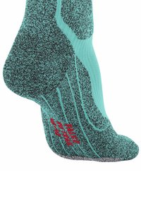 Nahaufnahme einer türkisfarbenen Socke mit strukturierten schwarzen Mustern und rotem Branding an der Sohle, die ihr sportliches Design und die Dämpfungseigenschaften zeigt.
