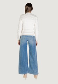 Giacca bianca trapuntata con motivo a zigzag, abbinata a jeans in denim blu a gamba larga. Tessuto morbido, design semplice e colori neutri.