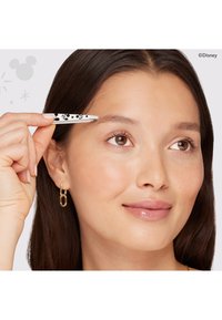 Pinzette mit weißem Griff und schwarzem Disney-Figurenmuster, von einer Hand in der Nähe einer Augenbraue gehalten; Modell hat mittelbraune Haare und goldene Ohrringe.