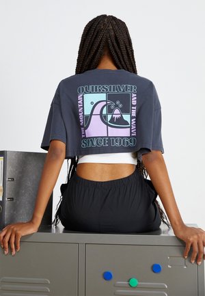 Skrojona granatowa koszulka z kolorowym wzorem logo przedstawiającym grafikę góry i fali. Połączona z czarnymi spodniami elastycznymi w pasie o gładkiej fakturze.