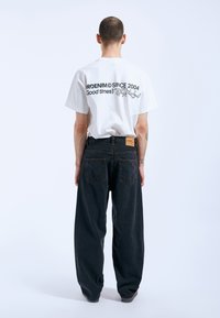 White graphic t-shirt with black text on the back, paired with loose-fitting dark denim jeans featuring visible back pockets and a label.