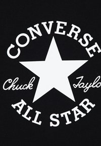 Svart tyg med en stor vit stjärna i mitten. Text som omger stjärnan: "CONVERSE," "Chuck," och "ALL STAR." Tydlig och kraftfull design.