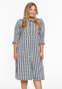 Hemdblusenkleid mit weißem Grund und schwarzem geometrischen Muster, langen Ärmeln mit elastischen Bündchen und einer lockeren Silhouette.
