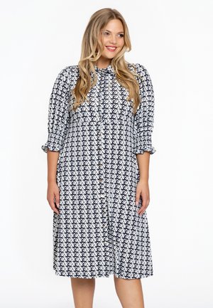 Hemdblusenkleid mit weißem Grund und schwarzem geometrischen Muster, langen Ärmeln mit elastischen Bündchen und einer lockeren Silhouette.