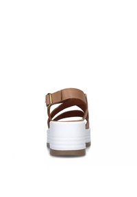 Sandali in pelle marrone con cinturini incrociati, suola piattaforma bianca, fibbia regolabile sul retro e superficie liscia.