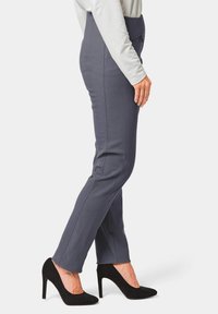 Graue, enganliegende Hosen mit vertikalen Nähten, kombiniert mit schwarzen Wildleder-Highheels. Die Hosen haben eine glatte Textur und ein elegantes Design.
