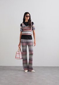 Šareni pleteni top s zigzag uzorkom i šire hlače, uparen s torbom s odgovarajućim uzorkom. Glatka tekstura i prilagođen stil.