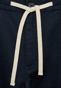 Navy blauwe broek met een trekkoord in de taille en een crèmekleurige katoenen strik. De stof heeft een gestructureerd uiterlijk en bevat een knoopdetail.