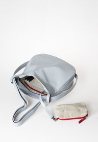 Grijze leren tas met een ronde ontwerp, voorzien van een enkele schouderriem en interne vakken. Inclusief een kleine beige pouch met rode accenten.