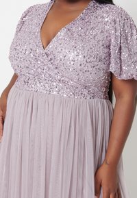 Lila klänning med paljetterad bodice, V-ringning och korta puffärmar; flödar ut i en plisserad, lätt kjol.