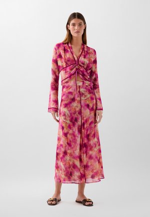 Fialovo-růžové tie-dye maxi šaty s dlouhými rukávy, výstřihem do V a shromažďováním vpředu, doplněné hnědými sandály se zlatým akcentem.