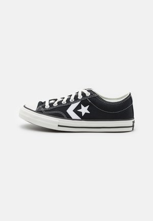 Zapatillas bajas de lona negra con cordones y detalles blancos, con un logo de estrella, puntera de goma y suela de goma blanca con franjas negras.