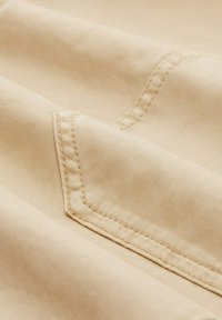 Beige fabric with a smooth texture, featuring visible stitching and a folded design. Hem details are clean and well-finished.