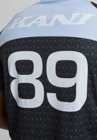 Juoda ir šviesiai mėlyna sportinė marškinėliai turi tekstūruotą audinį, didelį baltą "89" nugaros pusėje ir "KANI" atspausdintą viršuje.