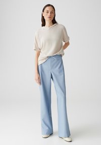 Felpa corta color beige, con maniche a giro e risvolto, abbinata a pantaloni larghi blu chiaro con vita regolabile tramite coulisse. Texture liscia, design casual.