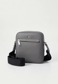 Borsa a tracolla in pelle grigia con finitura testurizzata, forma quadrata, tasca frontale con zip e tracolla nera regolabile. Logo esposto sul davanti.