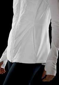Giacca sportiva bianca con texture trapuntata, zip completa e sottile apertura laterale. Maniche lunghe con fori per il pollice, tessuto liscio, design minimale.