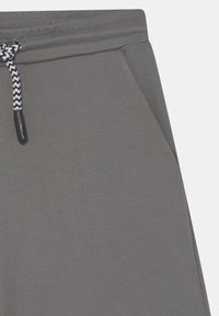 Szare dresowe spodnie z boku z kieszenią oraz czarno-białym sznurkiem do regulacji w elastycznym pasie.