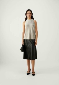 Silver sleeveless top paired with a black leather midi skirt. Model holds a black handbag, wearing black heels. Smooth textures, clean lines.