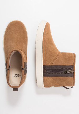 Paire de bottines en daim beige avec semelles blanches, fermetures éclair latérales et semelles intérieures de marque, vues de dessus et de côté sur fond blanc.