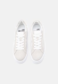 Ζευγάρι ανοιχτό μπεζ σουέντ αθλητικών παπουτσιών με λευκά κορδόνια και σόλες, με την επιγραφή "Love Moschino" στις εσωτερικές σόλες, σε θέαση από πάνω σε λευκό φόντο.