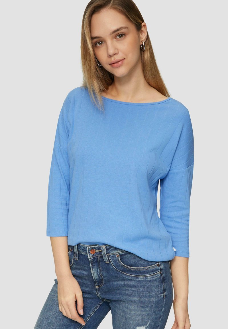 Helles blaues, geripptes Strickoberteil mit weitem Boottau-Ausschnitt und Dreiviertelärmeln, getragen mit Jeans. Glatte Textur, lässige Passform.