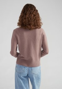 Texturiertes, leichtes Sweater in Mauve mit einem gerippten Saum, langen Ärmeln und Rundhalsausschnitt, kombiniert mit hellblauen, hochtaillierten Jeans.