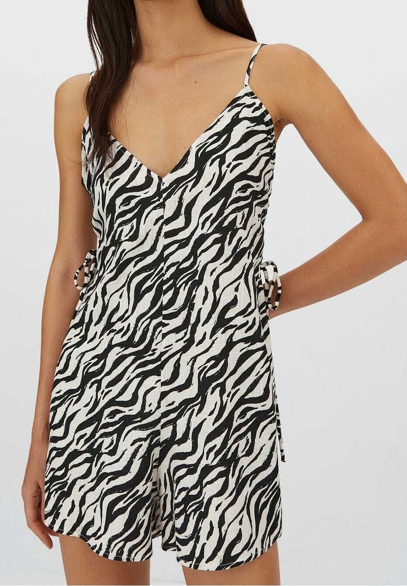 Femme portant un combishort sans manches à imprimé zèbre noir et blanc avec des bretelles fines et des détails de nœud sur le côté.