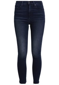Jeans skinny de tiro alto en azul oscuro con una textura suave, que presentan dobladillos deshilachados y un diseño tradicional de cinco bolsillos.
