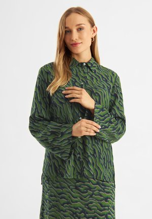 Green button-up shirt with wave pattern in dark green and navy, long sleeves, collar, and subtle sheen, paired with a matching skirt.