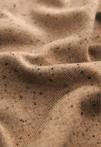 Tissu en tricot marron avec une surface texturée, parsemée de petites speckles noires. Le matériau semble doux et légèrement extensible.