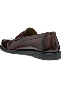 Mocassin en cuir bourgogne à enfiler avec un bout arrondi, des détails cousus et une semelle en caoutchouc noire. Texture lisse avec des accents minimalistes.