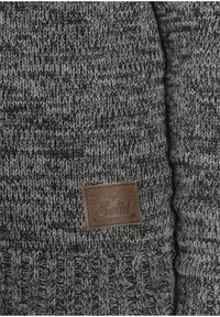 Jersey gris de punto con un diseño texturizado y una etiqueta de cuero marrón con la palabra "Solid" grabada. El material parece suave y cálido.