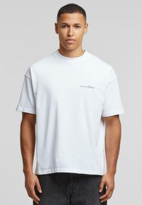 Hvid bomulds T-shirt med afslappet pasform. Den har korte ærmer og et lille blåt broderet logo på venstre brystområde.