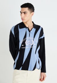 Sort og lyseblå stribet langærmet polo med sort krave, der har et hvidt logo designet på fronten. Blød strikket tekstur.