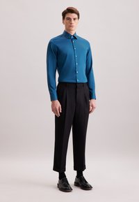 Teal shirt met lange mouwen en knoopsluiting, gecombineerd met zwarte geplooide broek en zwarte leren schoenen. Eenvoudig ontwerp, zonder patronen.