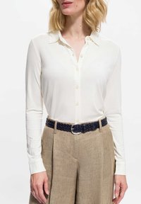 Biała bluzka z długim rękawem i kołnierzykiem, z przodu zapinana na guziki. Stylizowana z beżowymi, wysokim stanem spodniami i plecionym granatowym paskiem.