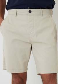 Bermudas de algodón beige con frente plano, bolsillos laterales y cierre de botón asegurado. Textura suave y corte recto a la altura de la rodilla.