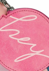 Ronde roze leren tas met een gestructureerd oppervlak, met het woord "hey" in witte cursieve letters langs de gebogen rand.