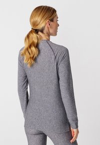 Camiseta gris de manga larga con un diseño ajustado, textura suave y mangas raglán, que presenta un escote redondeado y una parte trasera ligeramente más larga.