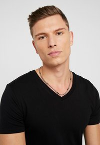 T-shirt noir à col en V en coton avec des manches courtes, porté avec un collier en perles argentées, mettant en avant un gros plan du décolleté.