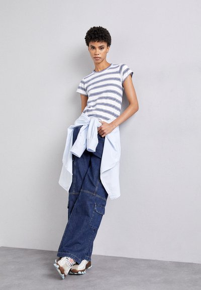 Tricou cu mânecă scurtă cu dungi în alb și marine, asortat cu pantaloni cargo lejeri din denim închis și o cămașă albastră deschis legată la brâu. Include adidași.